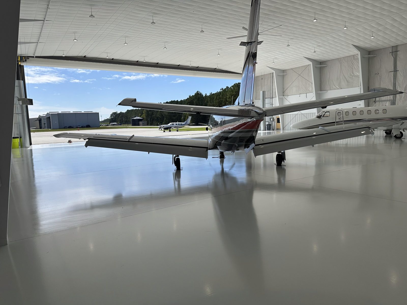 Two jets on the white floor looking out the open hangar door to the ramp